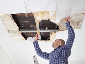 man cleaning water damage on his ceiling